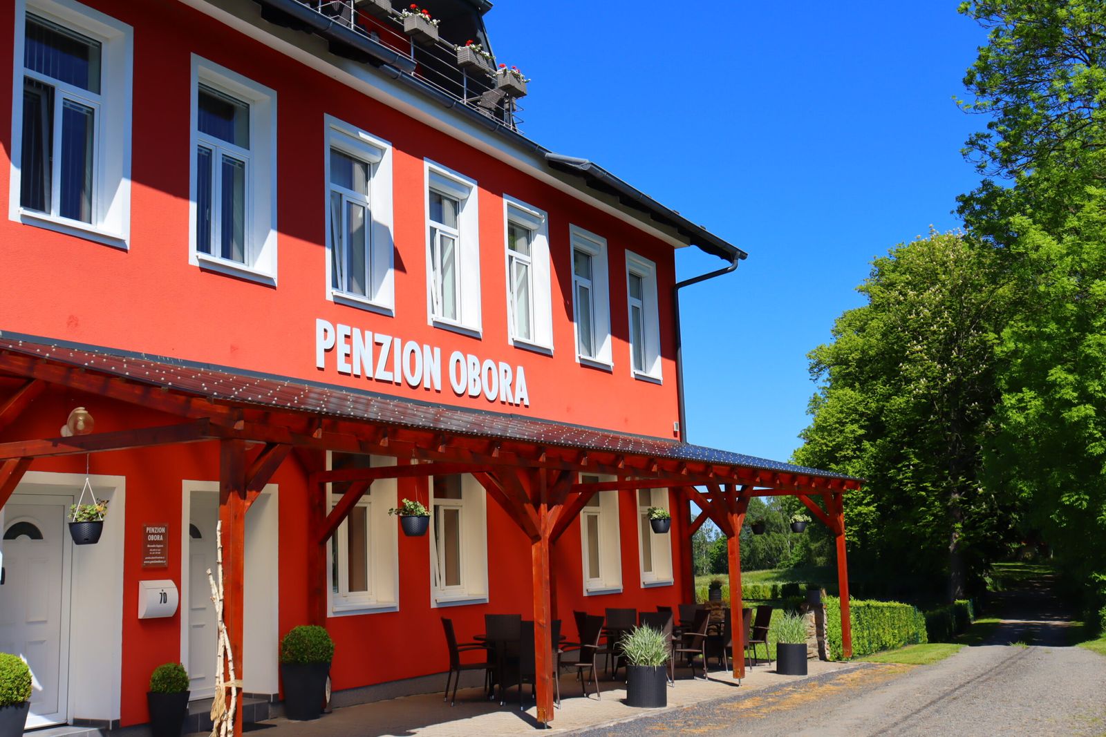 Penzion Obora — červená budova bývalé školy s dřevěnou pergolou