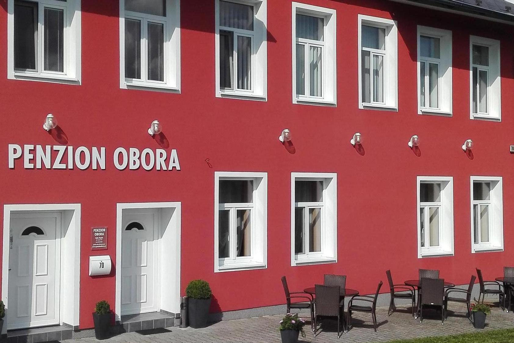 Červená fasáda penzionu Obora s posezením před budovou